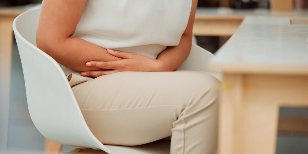 Closeup of one mixed race business woman holding sore tummy while feeling ill with menstrual stomac