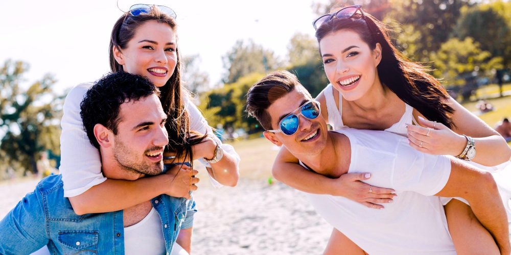 Group of young happy people carrying women on a sandy beach