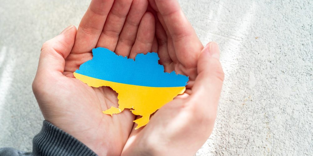 Hands holding national flag of Ukraine in the shape of the borders of Ukraine. Support for Ukraine