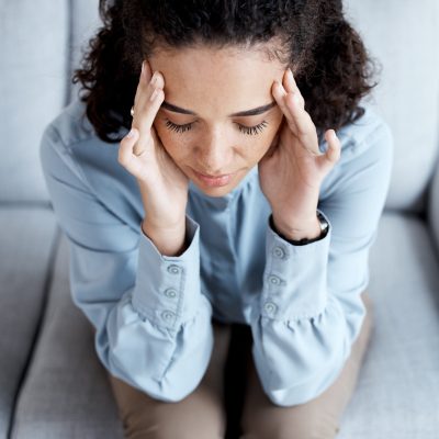 Headache, stress and anxiety with black woman on sofa for burnout, mental health and sad. Depressio