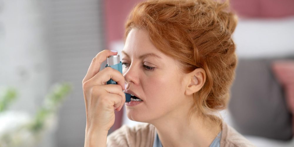 Red-haired woman opening mouth while using inhalator